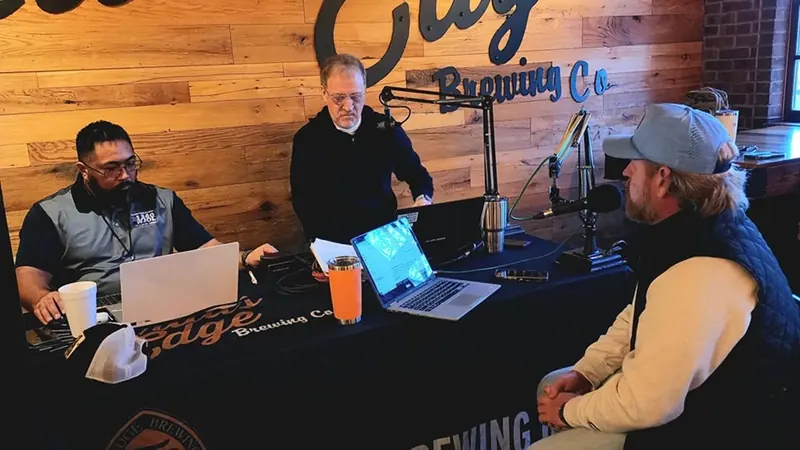 Three hosts at the 1340 AM WJOL broadcast table inside Trail’s Edge Brewing Co.
